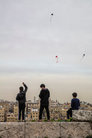 AMMAN, JORDAN - MARCH 12, 2019: Three children play with home-made kites on the walls of the ancient citadel of Amman, with the old city in the background.のeditorial素材
