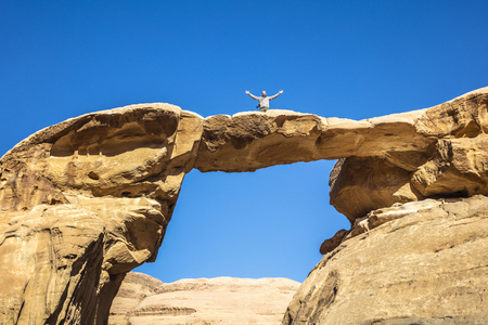 famous Um Frouth rock arch, located in the Wadi Rum desert in Jordan. Traveler photographer with open arms poses for a souvenir photo. happiness of being in a unique place in the world.の写真素材