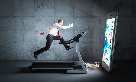 Businessman runs on a treadmill to feed a huge smartphone. Concept of technology addiction.