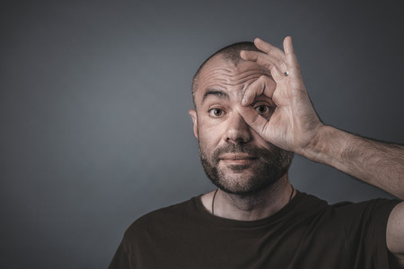 Portrait of a man looking through his fingers positioned to form a circle around his eye.の写真素材