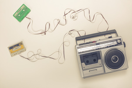 Old radio with tape recorder and cassettes with ribbon forming a wire. Flat lay style.
