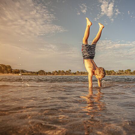 Caucasian child plays the vertical in the sea where the water is low, shot taken at sunset.