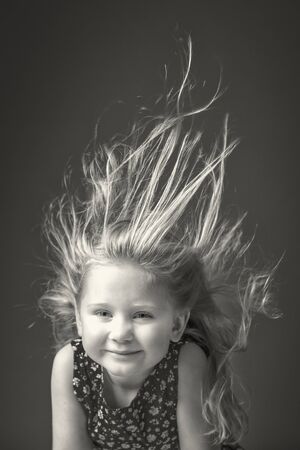 studio portrait of a 3 year old Caucasian girl with her hair raised in the air by the wind.の写真素材
