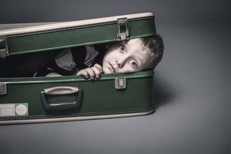 6 year old caucasian boy hides in an old suitcase, studio portrait.の写真素材
