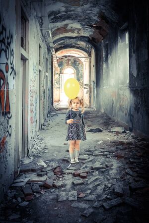 portrait of a 3 year old blonde girl with a balloon inside a decadent and abandoned building. Loneliness concept.の写真素材