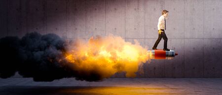 businessman above rockets causing a big flame and smoke. concrete background. concept of innovation, creativity, initiative, success.の写真素材