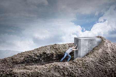 man pushes a huge concrete cube crawling into the ground. concept of determination and strength.