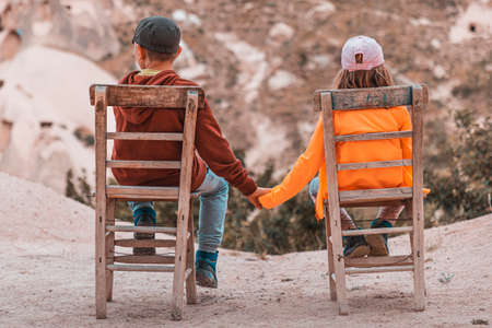 children sitting on wooden chairs holding hands, view from behindの写真素材