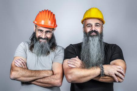 handymans with hard hat and crossed arms, long beards, studio shotの写真素材