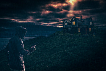 Man with a gun on a rainy day approaches a lonely houseの写真素材