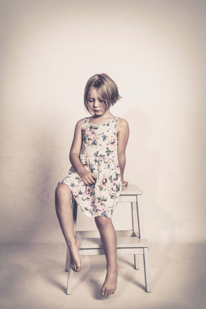 sad little girl sits on a stool looking at the floor