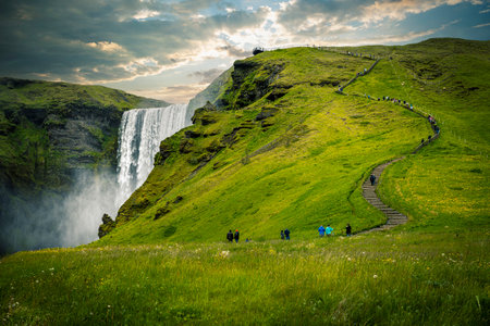 Tourists enjoying beautiful day hiking up path skogafoss waterfall icelandの写真素材