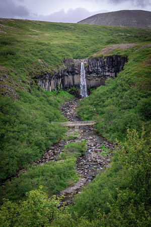Waterfall cascading down basalt columns in iceland's green landscapeの写真素材