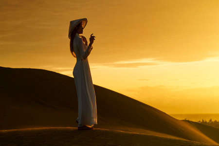 Ninh Thuan Province, Vietnam: portrait of a beautiful Vietnamese girl wearing a white ao dai on the sand dunes at dawnの写真素材
