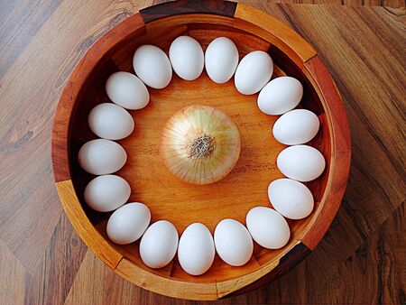 Eggs arranged in a circle with an onion in the center on a wooden surface.の写真素材
