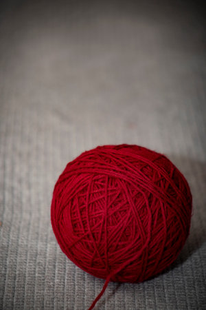 red ball of yarn on gray crocheted blanket with copy space, Craft hobby background with red yarn on...