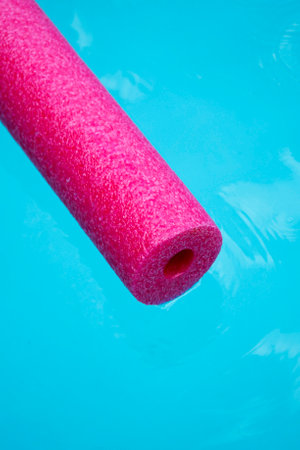 pink pool noodle floating on the blue waterの写真素材