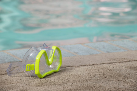 close up of children's yellow green swimming goggles sitting beside an indoor pool with copy space...