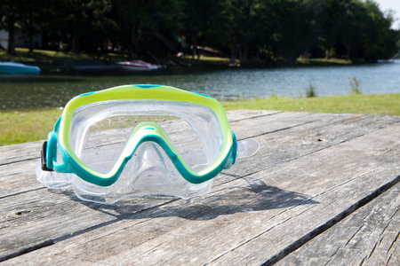 blue and yellow over the nose swimming goggles on the picnic table with the lake in the background....