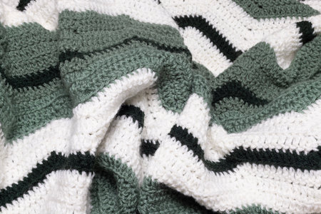 close-up of folded sage green zigzag blanket with white and hunter green accents, crocheted or knitted, reminds you of grandma's house, cozy and warm backgroundの写真素材