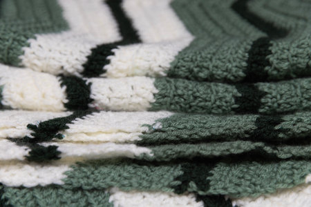 close-up of folded sage green zigzag blanket with white and hunter green accents, crocheted or...