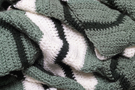 close-up of folded sage green zigzag blanket with white and hunter green accents, crocheted or...