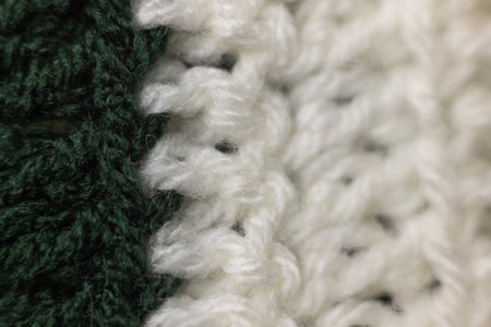 close-up of vertical rows of crochet stitches in a hunter green and white blanket, crocheted or...
