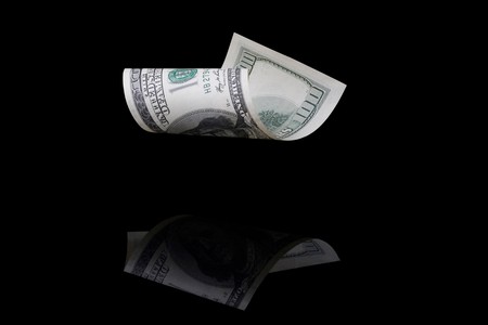 Falling hundred dollar bill on a black background with reflection