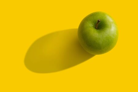 Green apple with shadow over yellow backgroundの写真素材