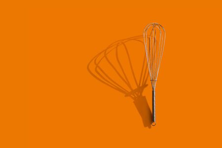 Stainless steel whisk with shadow over orange backgroundの写真素材