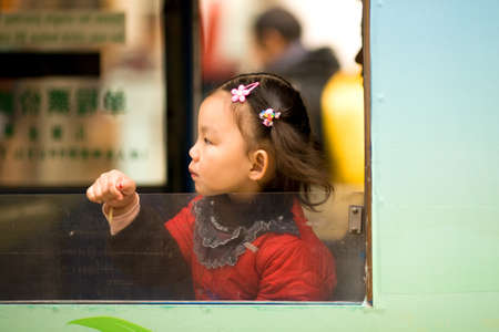 Shanghai, China, Asia - A Chinese little girl looking outside the window in a tram at Nanjing Road.のeditorial素材