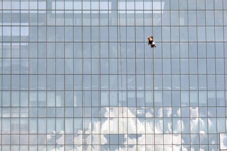 A brave man cleaning a mirror wall on high point in a big cityの写真素材