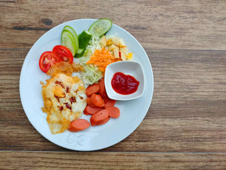 Breakfast with fried sausage,fried egg, vegetable and sauce in white plateの写真素材