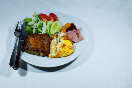 Breakfast with bread,fried egg,ham,and vegetables in white plate on white backgroundの写真素材