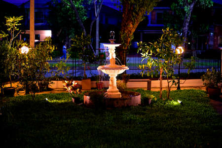 A fountain with water forms wine glass-shape on top on grass yard in the nighの写真素材