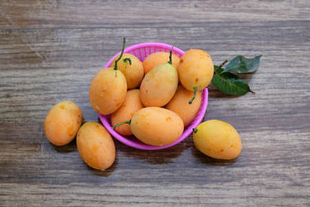 Sweet yellow Marian plums in overwhelming pink basket on wood table
