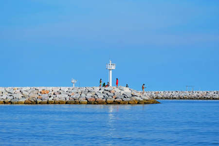 Travelers do activities on rock road extended to the sea near white lighthouses under blue sky backgroundの写真素材