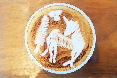 Hot coffee covered with cream dropping a figure of white horse and leaf stick on surface in white cupの写真素材