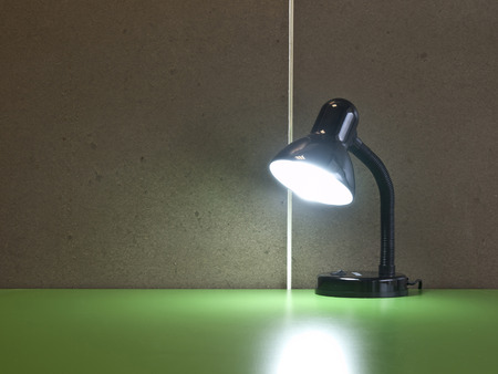 The black table lamp on the green desk in front of cement wall backgroundの写真素材