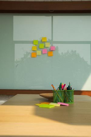 Conference room with colorful writing equipment on wooden desk and note pad on glass wall.の写真素材