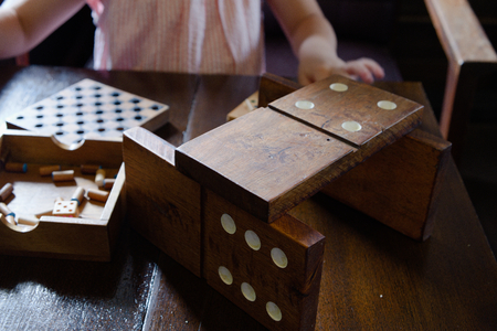 One child is playing a jiant dominoes made of wood and other toys on an old wooden table.の写真素材