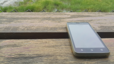 The cell phone is placed on a wooden table that can sit on the rice field in the rainy season.の写真素材