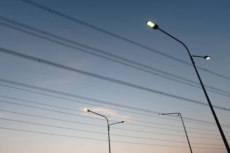 Electric pole with LED lighting. The light is emitting at dusk and there are many high voltage...