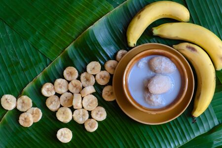Traditional Thai dessert: Fresh bananas are peeled and cut into pieces and placed on a brown plate. And Thai desserts made from bananas and coconut milk placed on a green banana leaf background,の写真素材