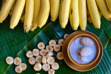 Traditional Thai dessert: Fresh bananas are peeled and cut into pieces and placed on a brown plate. And Thai desserts made from bananas and coconut milk placed on a green banana leaf background,の写真素材