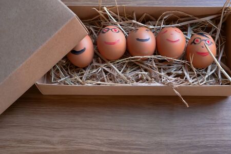 Several eggs that were written as smiling faces were placed in a brown box on a wooden table.の写真素材