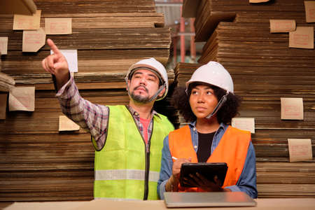 African American Female worker in a safety uniform and hard hat and male colleague inspect storage,...