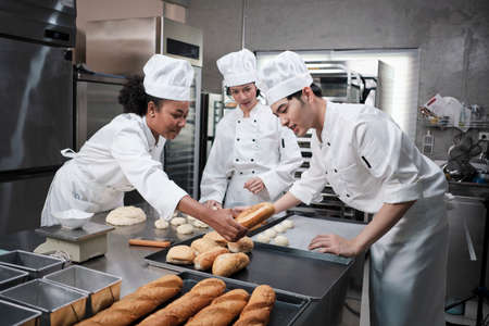 Professional gourmet team, three young chefs in white cook uniforms and aprons knead pastry dough...