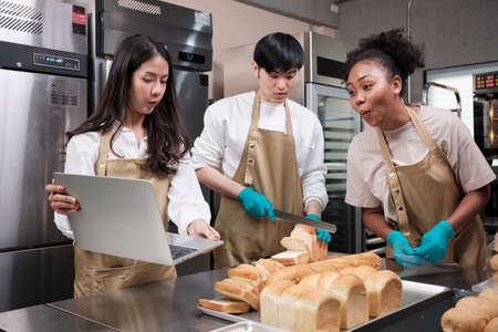 Three young friends and startup partners of bread dough and pastry foods busy with homemade baking jobs while cooking orders online, packing, and delivering on bakery shop, small business entrepreneur.の写真素材