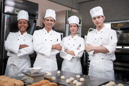 A Group of multiracial professional happy chefs team staff in white cooking uniforms stands in a row, arms crossed with confidence, cheerful smiles with commercial culinary jobs in restaurant kitchen.の写真素材